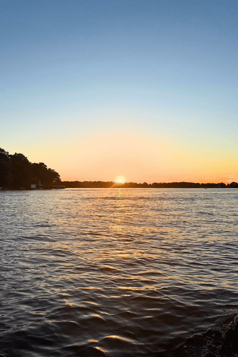 Sunset over Okauchee Lake in Wisconsin with calm water and a blue sky.